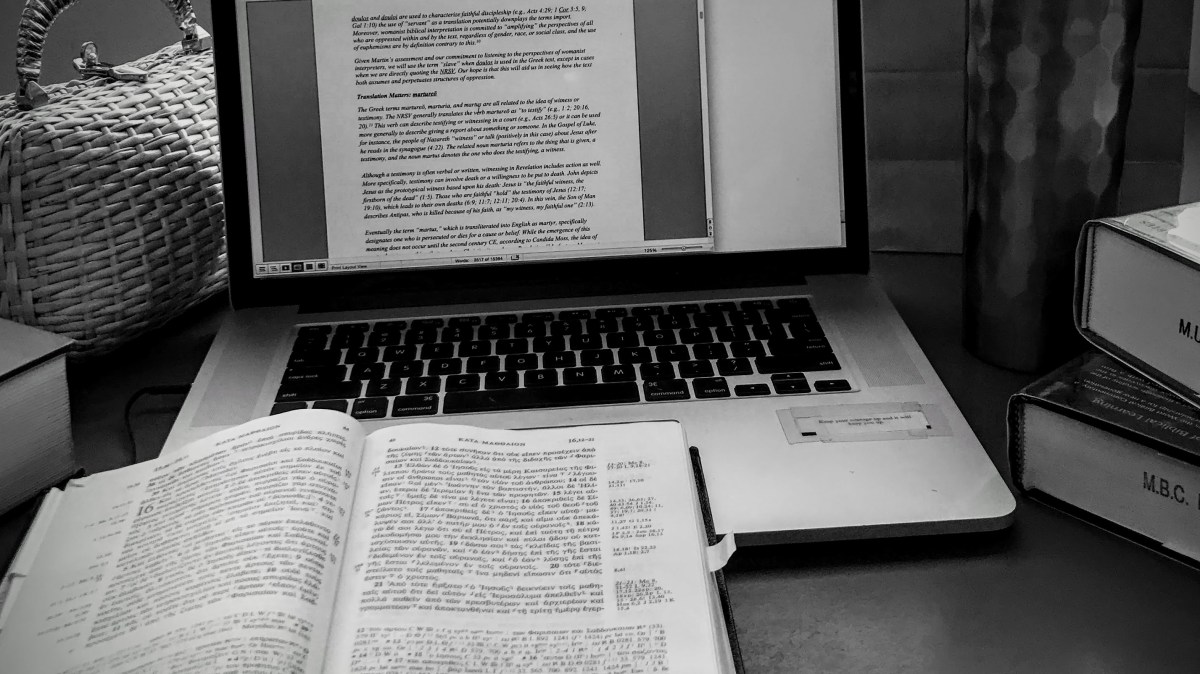 Black and white picture of laptop with writing and an open book.