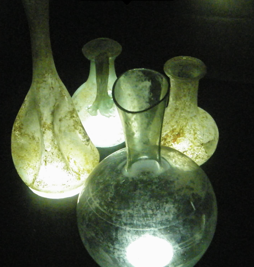 Green and blue vases that are glowing from a light shining underneath them. The background is black.